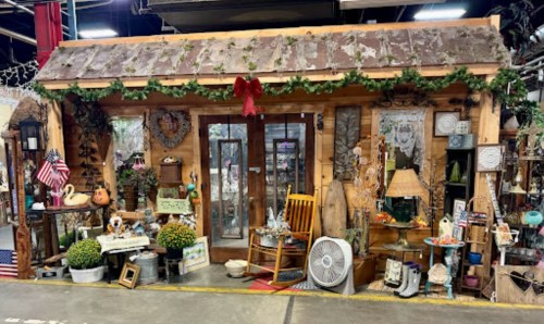 A rustic wooden shop front decorated with greenery, vintage items, and a welcoming porch.