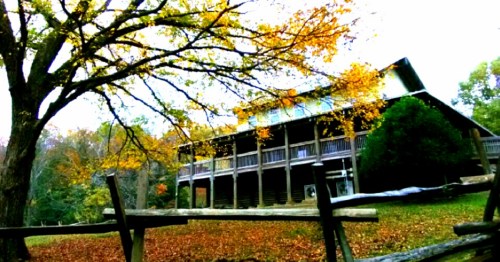 A rustic wooden lodge surrounded by autumn foliage and a wooden fence, set in a serene natural landscape.