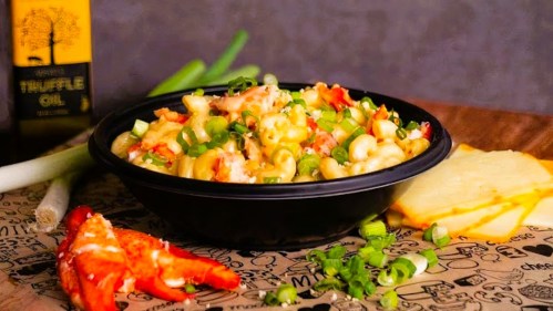 A bowl of creamy pasta with lobster, topped with green onions, alongside truffle oil and cheese slices.