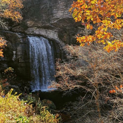 A serene waterfall cascades down rocky cliffs, surrounded by autumn foliage in vibrant orange and yellow hues.