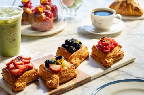 A selection of pastries topped with fresh fruit, served with coffee and a green drink on a marble table.