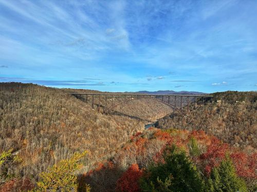 A scenic view of a bridge spanning a valley with autumn foliage and a blue sky in the background.