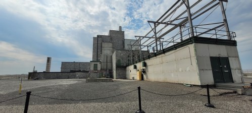 Abandoned industrial building with a gray exterior and metal framework, set against a cloudy sky.