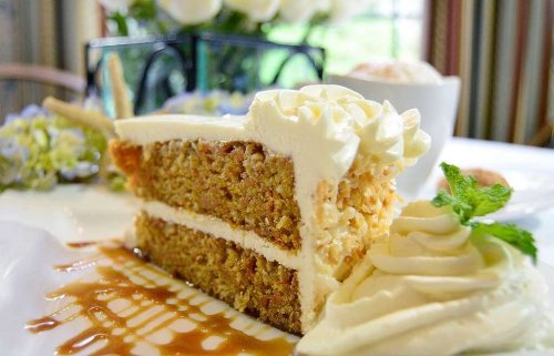 A slice of layered cake with cream frosting, garnished with mint, served on a plate with caramel drizzle.
