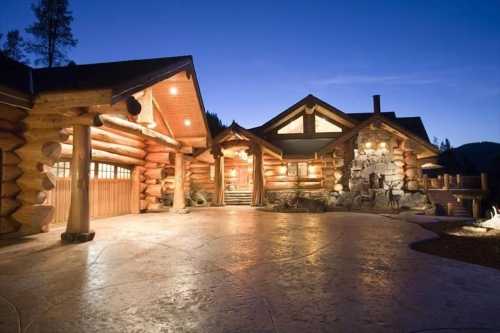 A rustic log cabin at dusk, featuring a spacious entrance and stone accents, surrounded by trees.