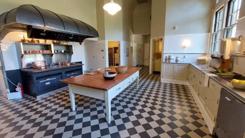 A spacious kitchen with a large central island, checkered floor, and modern appliances, featuring a vintage stove.