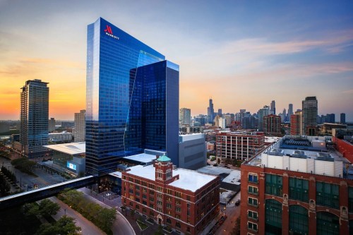 Aerial view of a modern Marriott hotel in a city skyline at sunset, showcasing glass architecture and surrounding buildings.