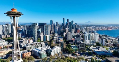 Aerial view of Seattle skyline featuring the Space Needle, with Mount Rainier in the background and a clear blue sky.