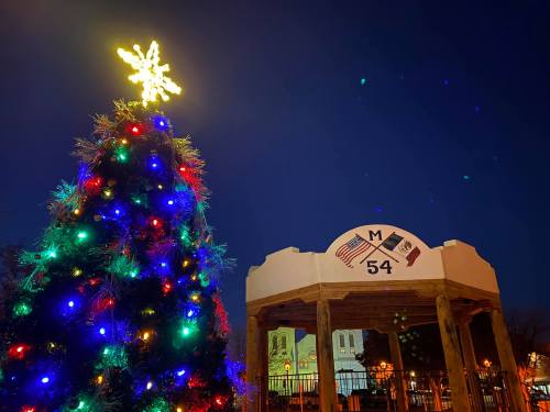 A brightly lit Christmas tree with colorful lights beside a gazebo featuring a star and decorative elements at night.