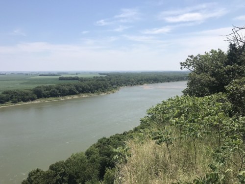 A scenic view of a river winding through lush green landscapes under a clear blue sky.