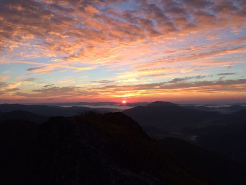 A vibrant sunrise over mountains, with colorful clouds and a misty valley below.