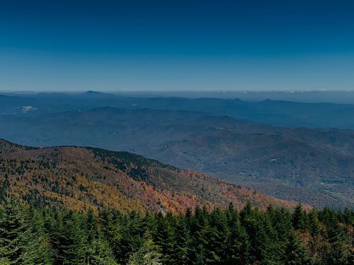 A panoramic view of mountains with autumn foliage under a clear blue sky.