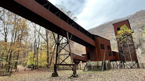 Abandoned industrial structure surrounded by autumn trees and mountains under a cloudy sky.
