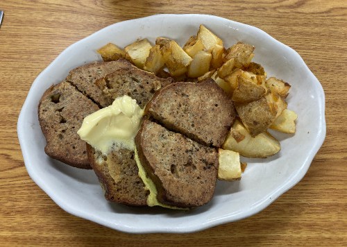 A plate with sliced brown bread topped with butter, accompanied by golden-brown potato cubes.