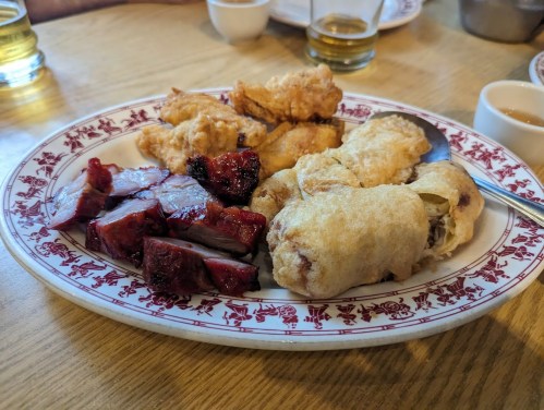 A plate of assorted fried meats, including crispy chicken and barbecued pork, served with dipping sauce.