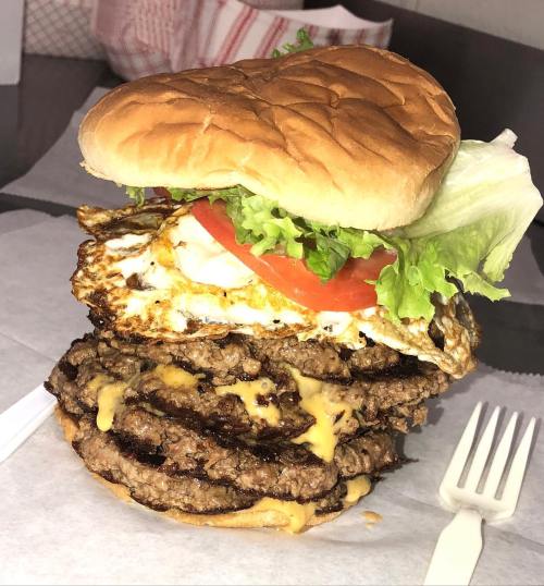 A towering burger with multiple beef patties, melted cheese, lettuce, tomato, and a fried egg on a bun.