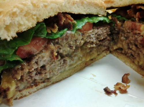 Close-up of a juicy burger with lettuce, tomato, cheese, and bacon, cut in half to reveal its layers.