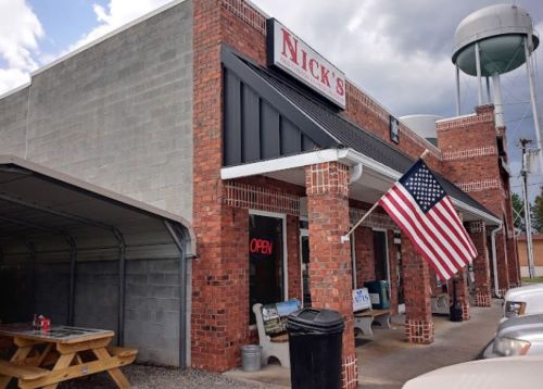 A brick building with a sign reading "Nick's," featuring an American flag and an "Open" sign in the window.
