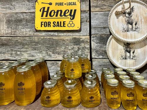 Bottles of honey displayed on a wooden shelf with a sign reading "Pure Local Honey for Sale" and decorative plates.