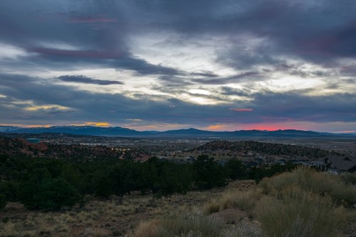 A scenic view of a valley at sunset, with mountains in the distance and a colorful sky filled with clouds.