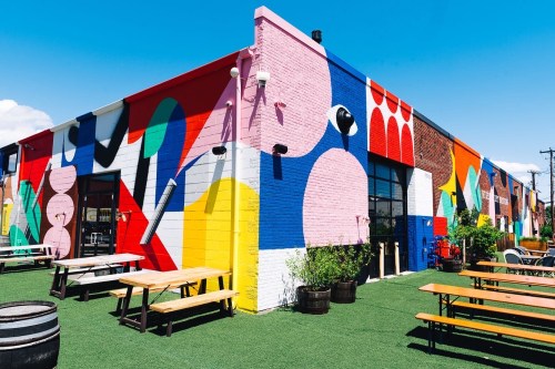 Colorful mural on a building exterior with outdoor seating and greenery in a vibrant urban setting.