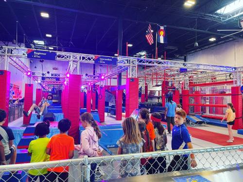 A vibrant indoor gym with kids watching as others navigate obstacle courses and climbing structures.