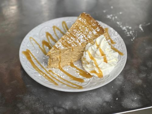 A slice of caramel cake on a plate, drizzled with caramel sauce and served with a dollop of whipped cream.
