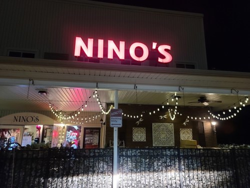 A restaurant named "Nino's" illuminated at night, with string lights and an "Open" sign visible.