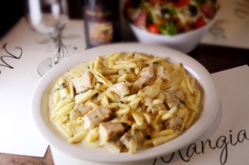 A plate of creamy pasta with chicken, served alongside a fresh salad in a restaurant setting.
