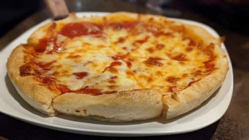 A freshly baked pizza with a golden crust, topped with melted cheese and pepperoni slices, served on a white plate.