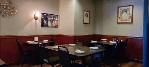 Cozy restaurant interior with empty tables, black chairs, and framed artwork on the walls. Warm lighting creates a welcoming atmosphere.