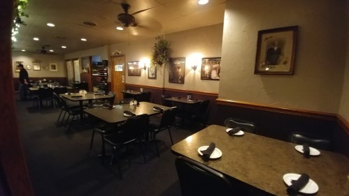 Interior of a restaurant featuring empty tables, dark decor, and framed photos on the walls.