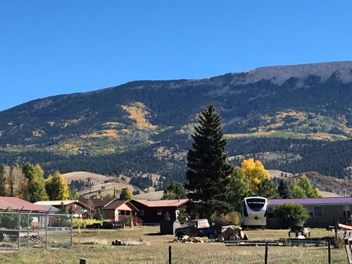 A scenic view of a mountain with autumn foliage, overlooking a small town and a clear blue sky.