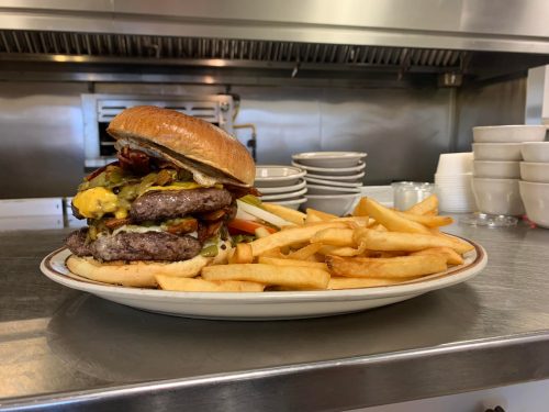 A towering burger with multiple patties, cheese, and toppings, served with a side of golden French fries on a plate.