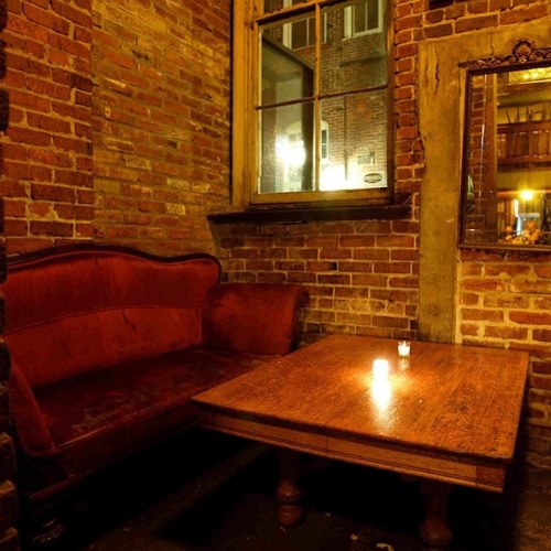 Cozy interior of a dimly lit room featuring a red velvet couch and a wooden table with a candle.