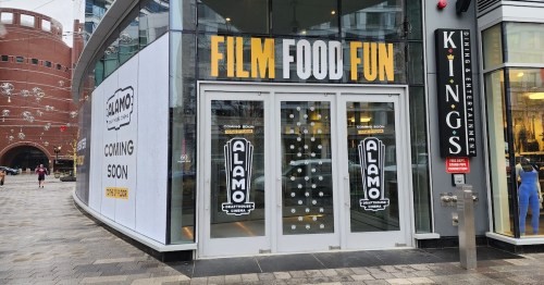 Exterior of a building with signs for "Alamo" featuring "Film Food Fun" and "Coming Soon" announcements.