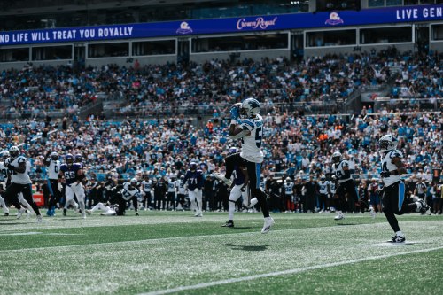 A football player leaps to catch a pass during a game, with a cheering crowd in the background.