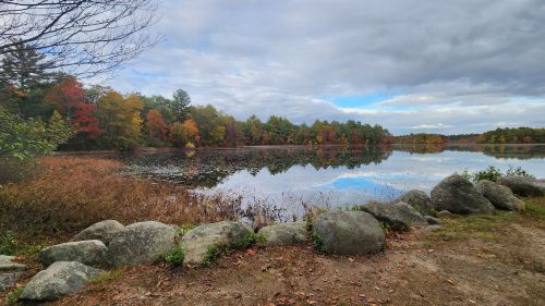 A serene lake surrounded by colorful autumn trees, with a cloudy sky reflecting on the water's surface.