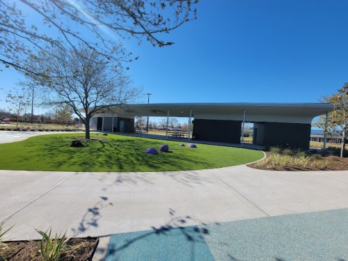 A modern building with a curved roof, surrounded by green grass and trees under a clear blue sky.