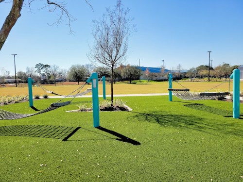 Two hammocks suspended between blue posts on a grassy park area under a clear blue sky.