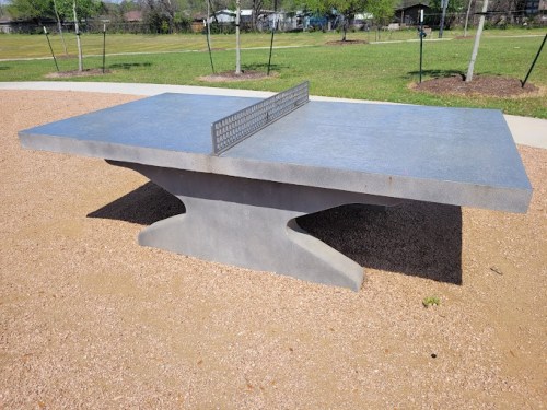 A concrete table tennis table in a park, surrounded by grass and trees.