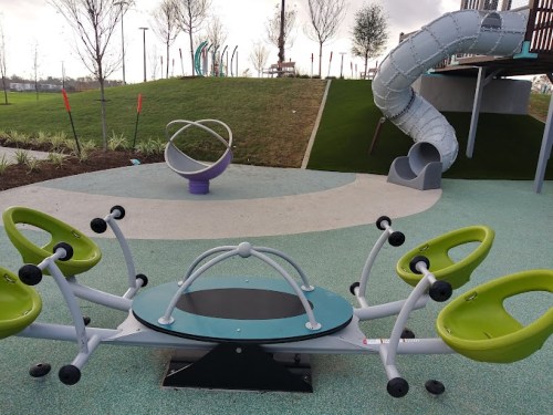 A colorful playground featuring a spinning ride, a slide, and a unique seating structure on a grassy area.