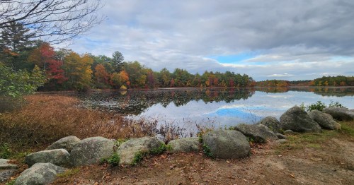A serene lake surrounded by autumn foliage and rocky shoreline under a cloudy sky.