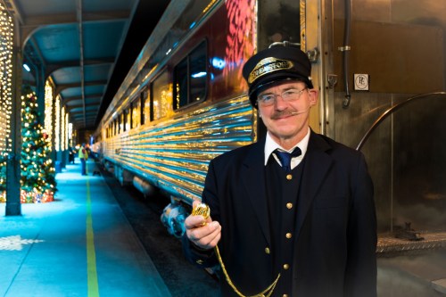 A train conductor in uniform holds a pocket watch, standing beside a beautifully decorated train platform.