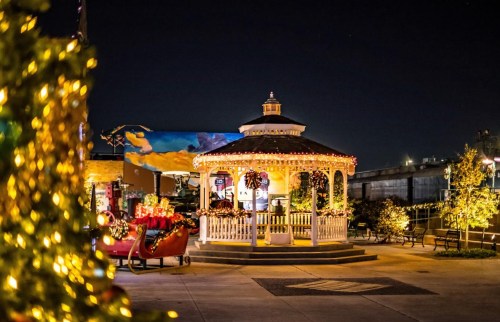A beautifully lit gazebo decorated for the holidays, surrounded by festive lights and a Christmas tree at night.