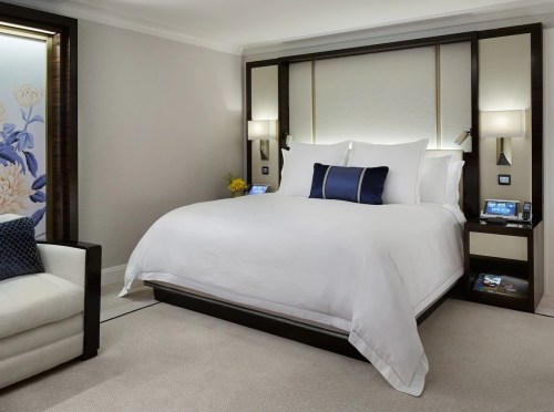 A modern hotel room featuring a large bed with white linens, decorative pillows, and stylish lighting.