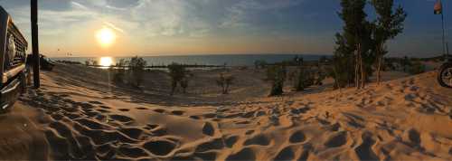 A panoramic view of a sandy beach at sunset, with trees and calm water in the background.