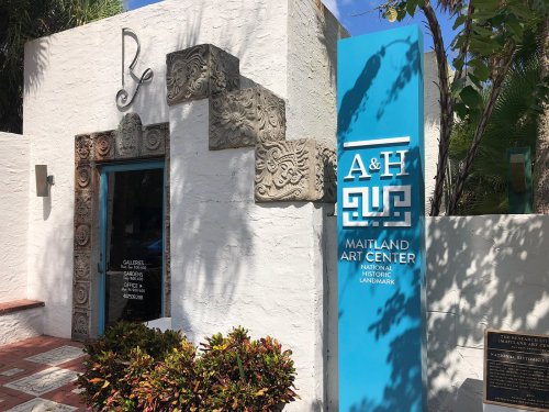 Exterior of the Maitland Art Center featuring a blue sign and decorative stonework on a white building.