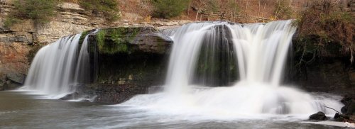 A serene waterfall cascading over rocky cliffs into a calm river, surrounded by lush greenery and autumn foliage.