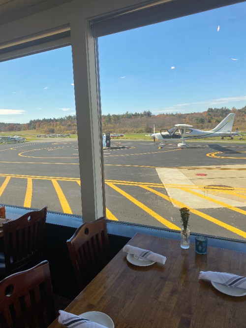 View from a restaurant window showing a small airport runway with parked planes and a clear blue sky.
